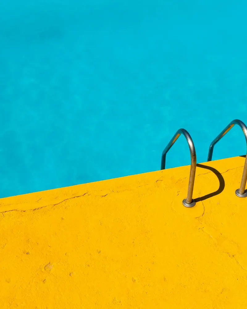 Blue swimming pool with a steel ladder and a yellow deck